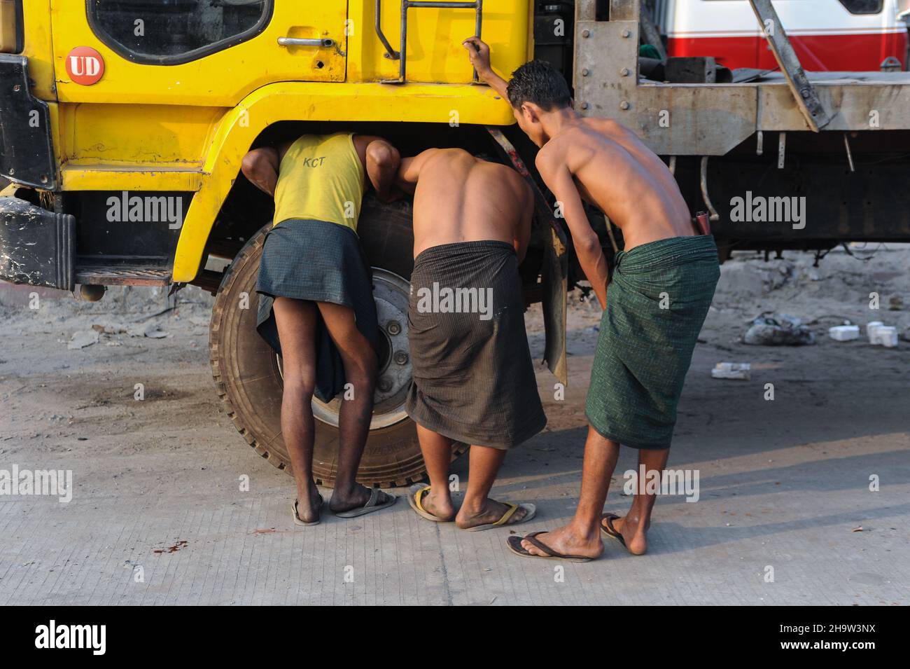 '10.02.2014, Myanmar, , Yangon - Three young workers in traditional wraparound skirts (longyi) inspect a defective truck at the roadside.. 0SL140210D0 Stock Photo