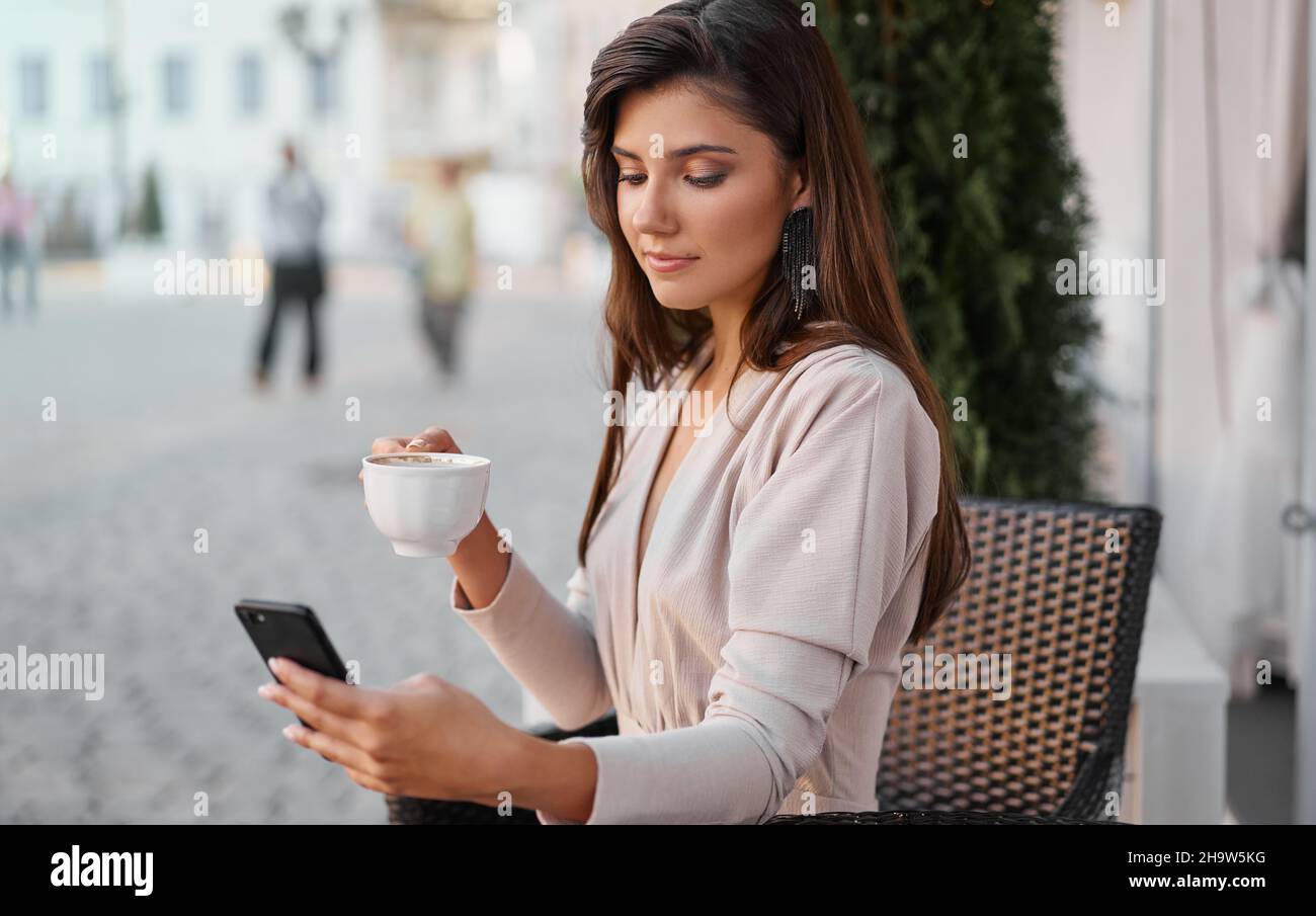 Young beautiful woman with smartphone sitting in the street cafe with coffee. Concept meeting, working, freelance Stock Photo