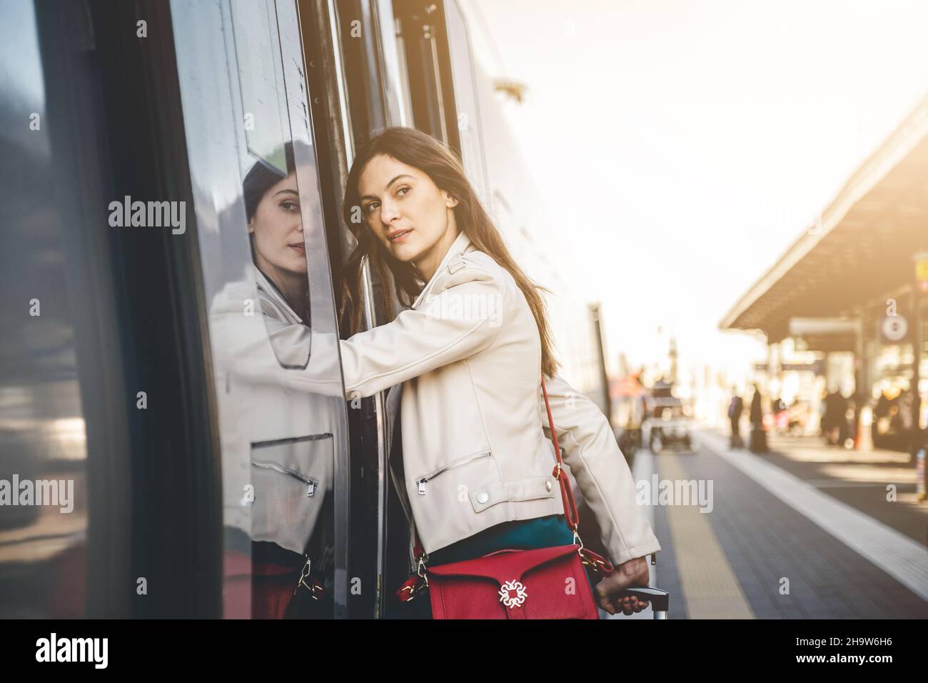 Young business woman standing on train door peeking out looking for somebody in railway station - Potrait of beautiful traveler woman getting on the t Stock Photo