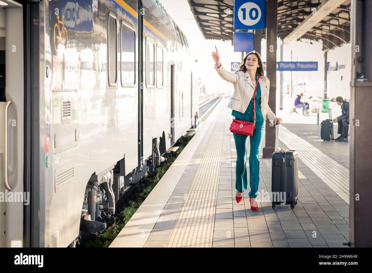 Beautiful girl running and chasing the leaving train in station. Waving hand and rushing to get on - Young business woman with suitcase running Stock Photo