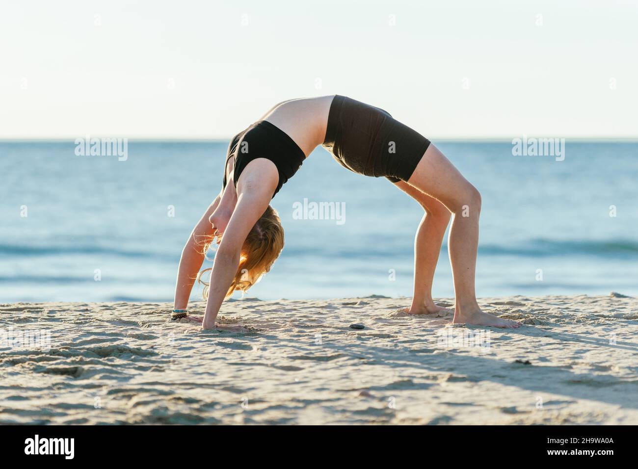 Woman doing the bridge position of yoga on a beach Stock Photo