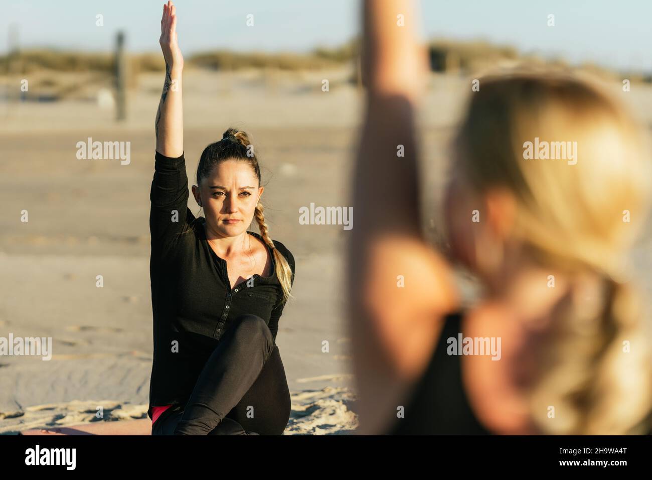 Woman raisin arm while doing a yoga class on the beach Stock Photo