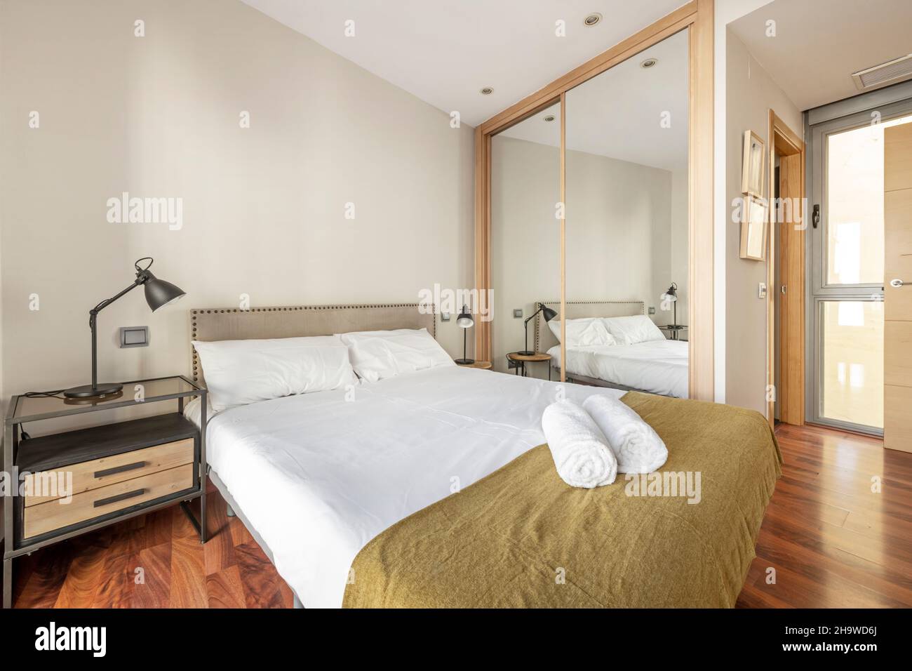 nice bedroom with king size bed, built in wardrobe with mirrored doors and en suite bathroom in a vacation rental apartment Stock Photo