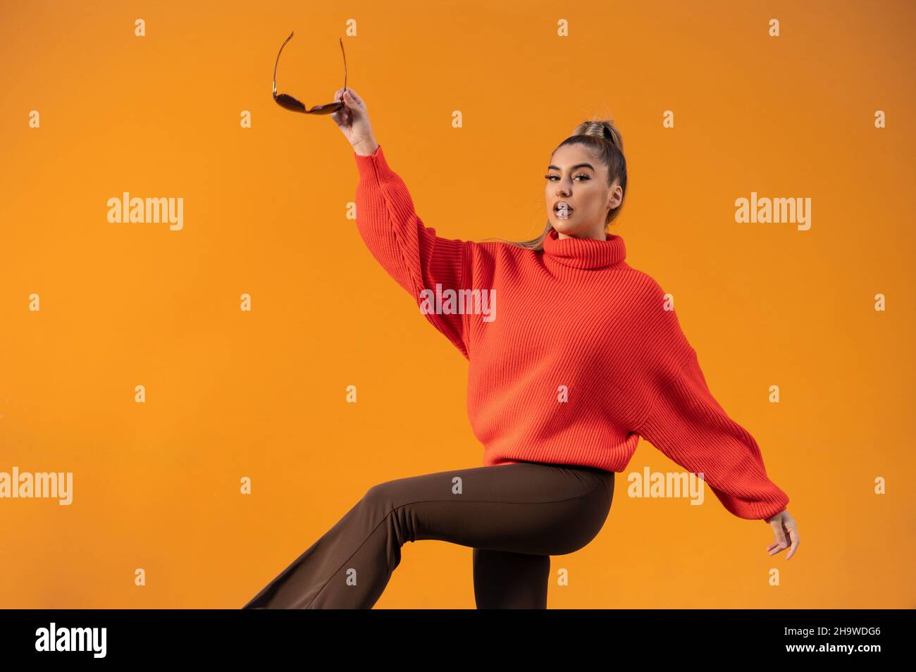Stylish female posing in the orange background is wearing a bright sweater Stock Photo