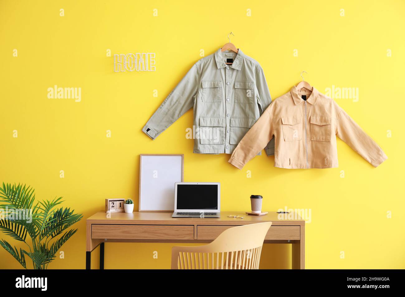Comfortable workplace with modern laptop and stylish jackets hanging on color wall in room Stock Photo