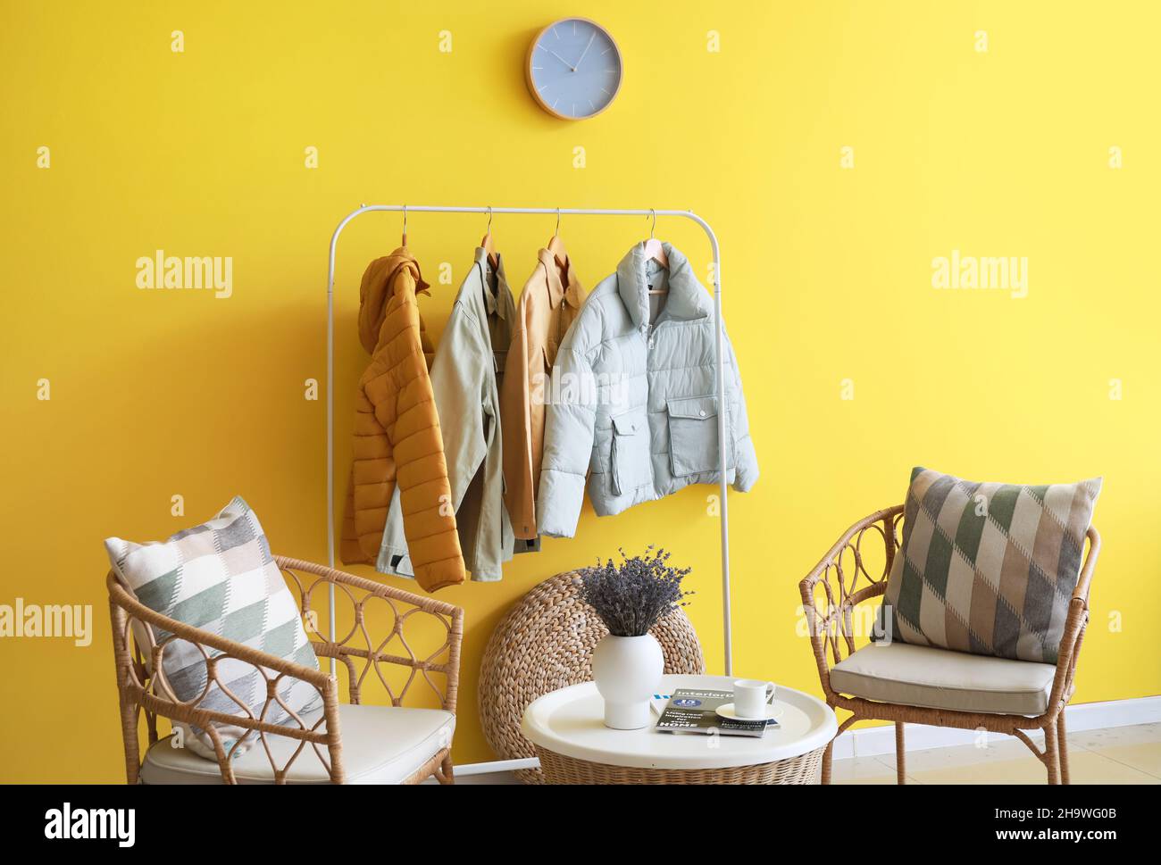 Comfortable chairs and hanger with jackets near color wall in room interior Stock Photo
