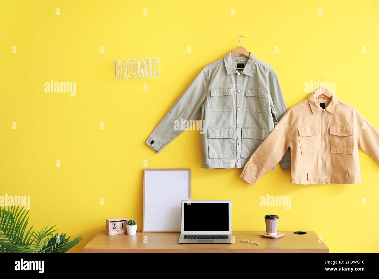 Comfortable workplace with modern laptop and stylish jackets hanging on color wall in room interior Stock Photo