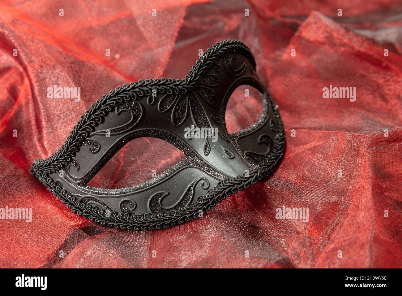 Carnival Venetian mask black with glitter on red textile background. Traditional festival female disguise, masquerade Stock Photo