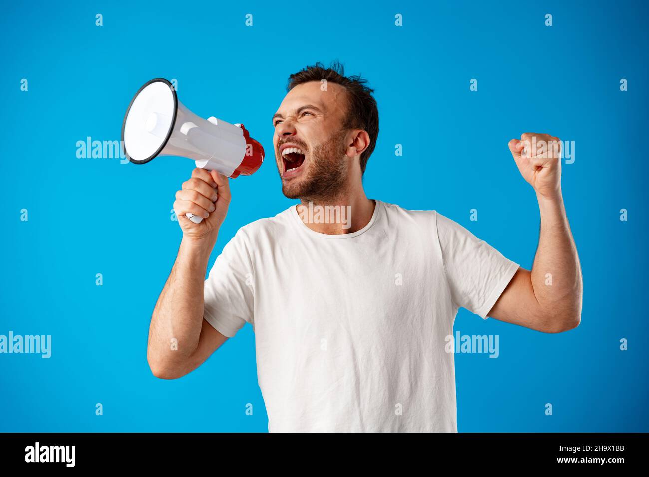 Handsome man over blue wall shouting through a megaphone. Stock Photo