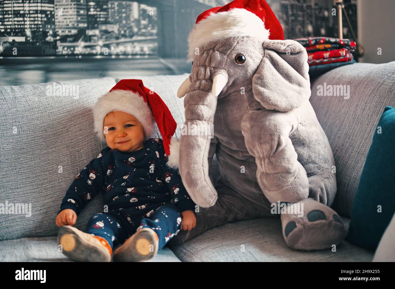 Cute little boy in Christmas costume and Santa hat with stuffed elephant sitting on a sofa Stock Photo