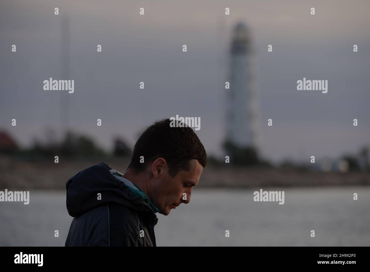 upset sad man head down near sea coast with lighthouse on background Stock Photo