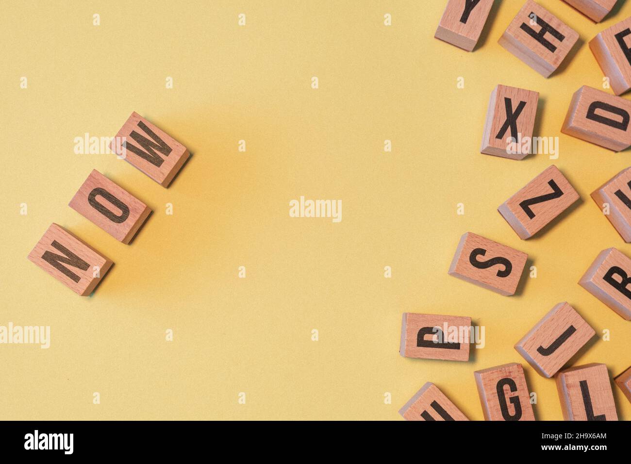 Word NOW, taken from a pile of wooden letter blocks with yellow ...