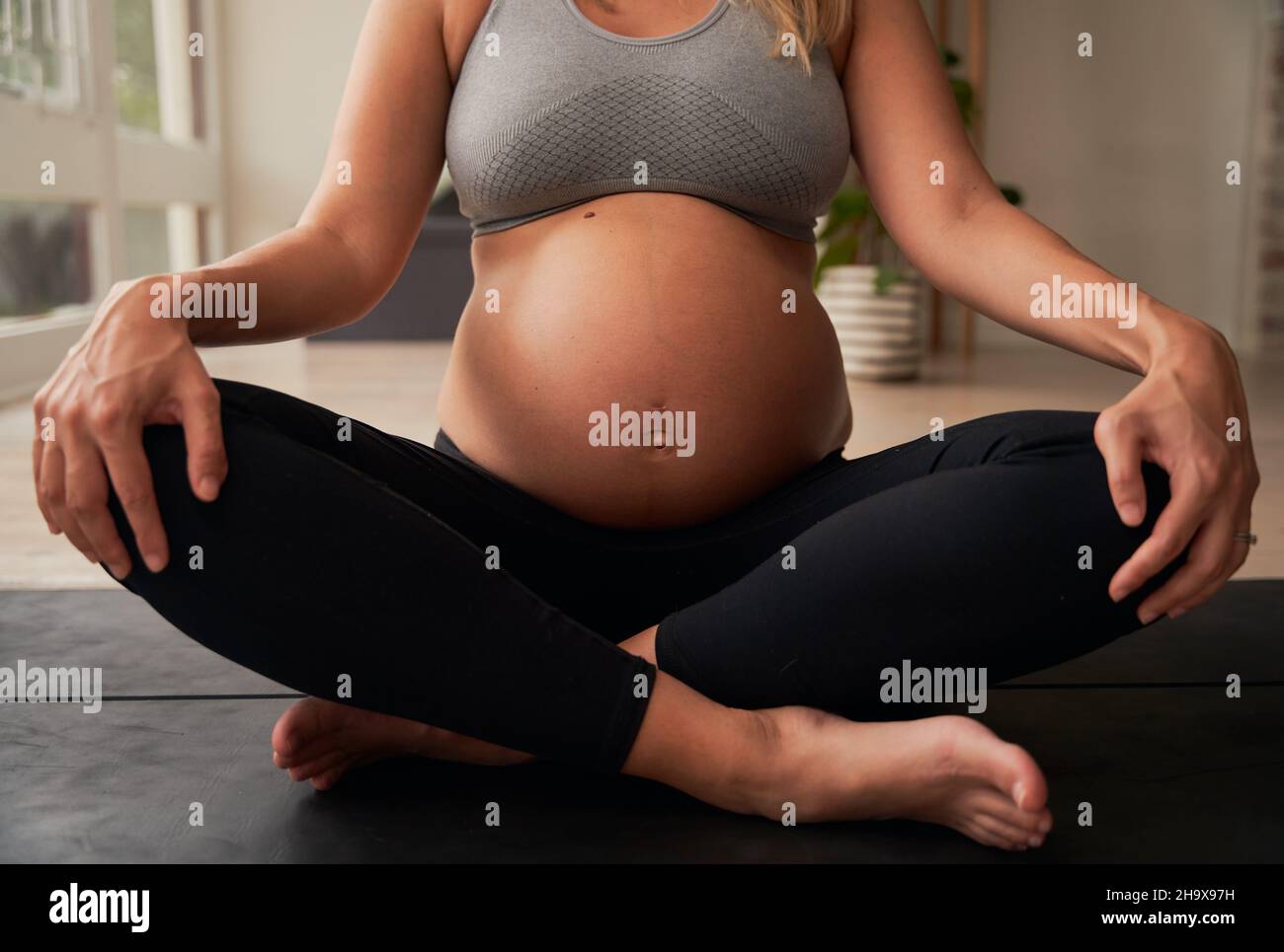 Caucasian female pregnant mother sitting on yoga mat practising breathing exercises Stock Photo