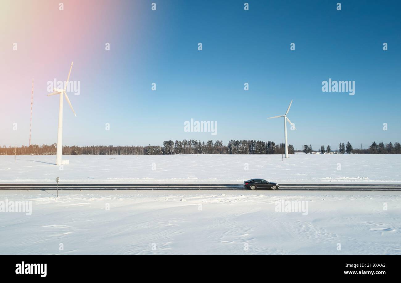 Car moving on snowy road with blue sky and electric wind plant background Stock Photo