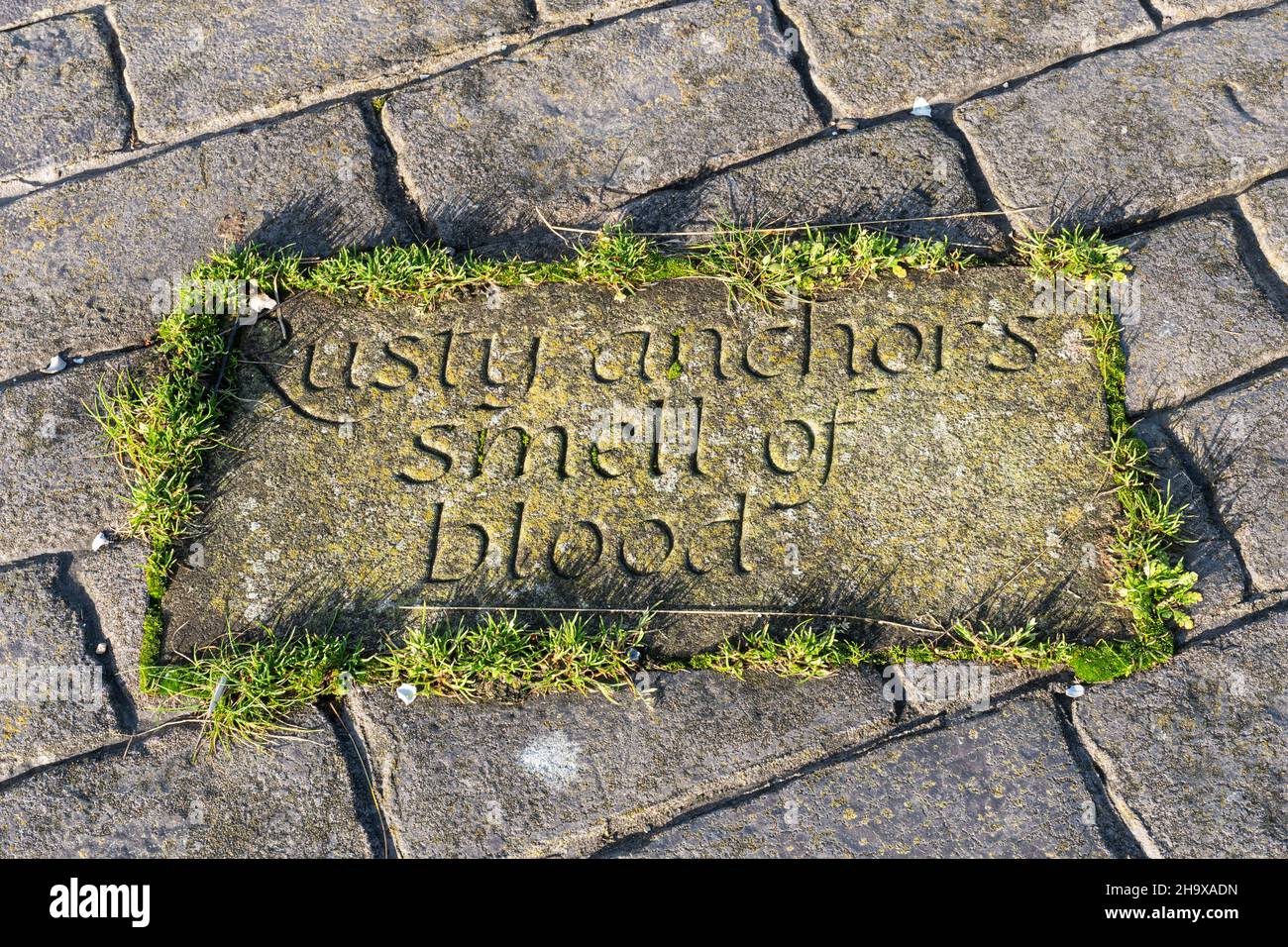 Carved stone slab in the harbour wall at Maryport with the words 'Rusty anchors smell of blood', Cumbria, England, UK Stock Photo