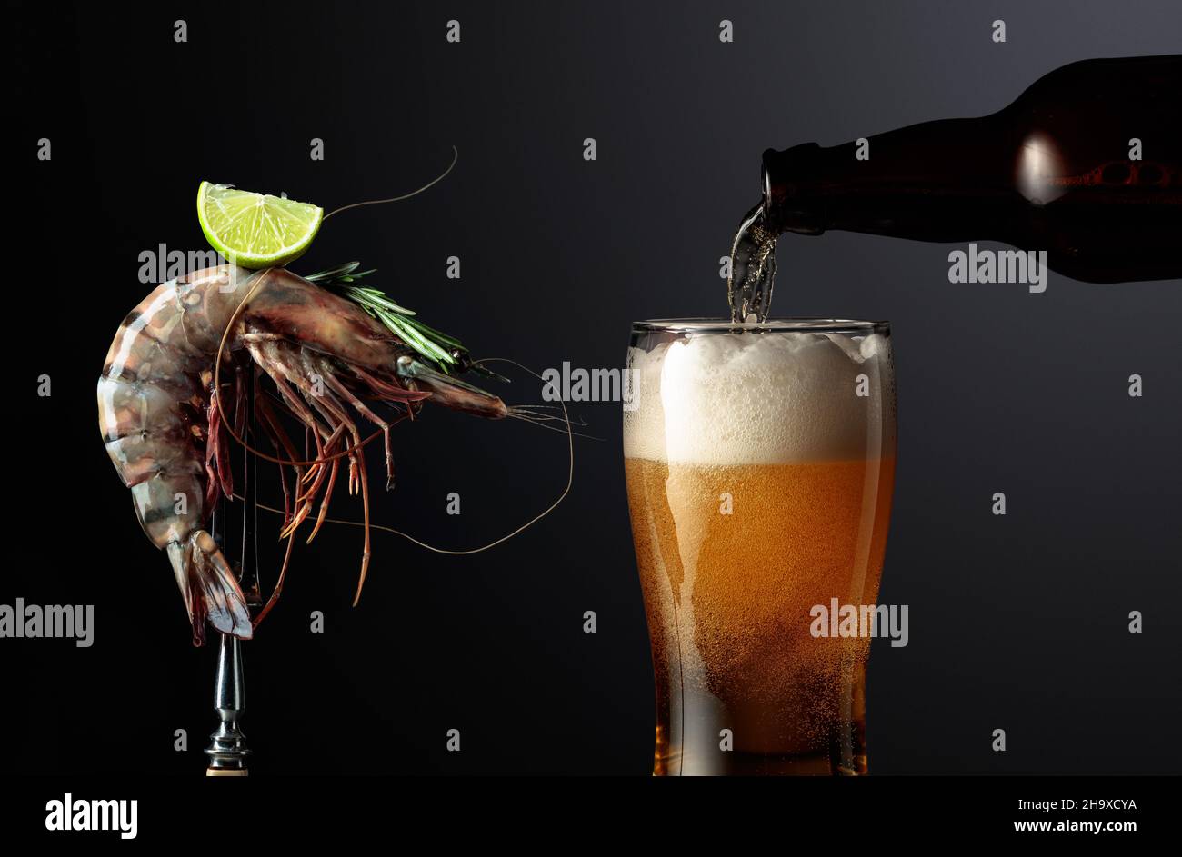 Beer and fresh tiger prawn with rosemary and lime slice on a black background. Copy space. Stock Photo