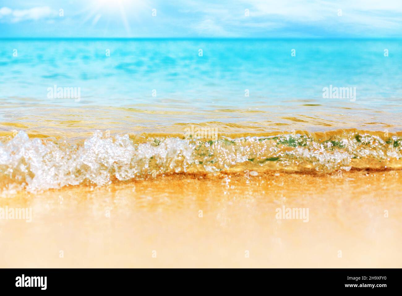 Tropical island beach nature, blue sea wave splash closeup, turquoise ocean water, yellow golden sand, sun sky, white clouds, summer holidays backgrop Stock Photo