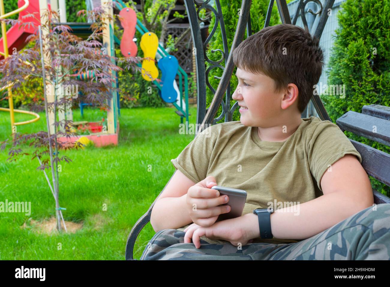 A boy with a phone and smart watch in the backyard Stock Photo