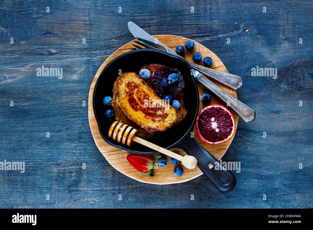 Homemade Cinnamon French Toasts with honey, berries and bloody orange in vintage cast iron pan for breakfast on rustic wooden background Stock Photo