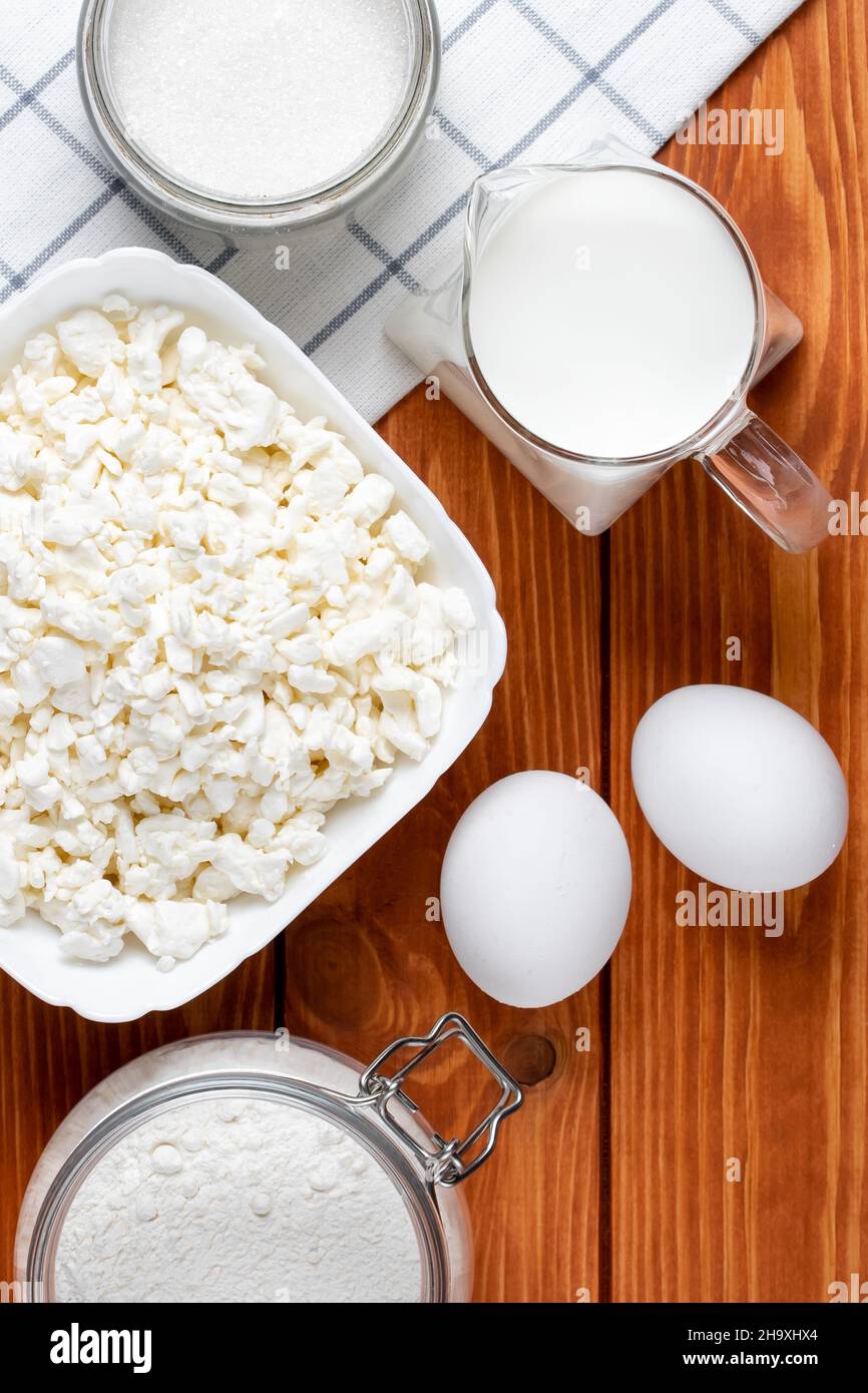 Ingredients for baking on a brown wooden table, cooking. Eggs, flour, cottage cheese, sugar and milk on the boards background. Top view, flat lay. Clo Stock Photo