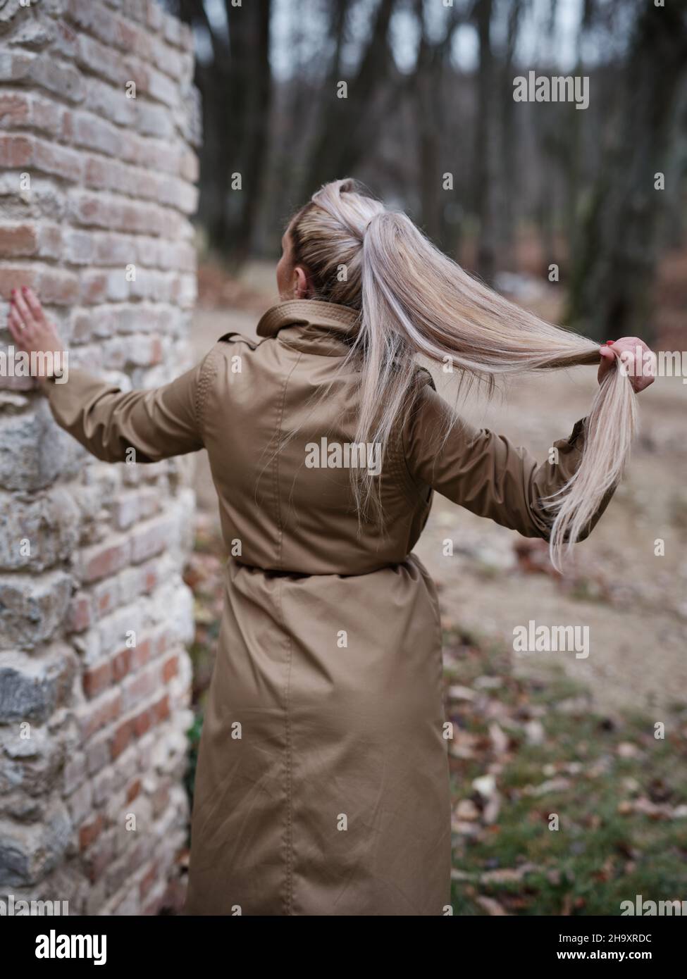 Rear view of a young woman in a beige coat outside leaning against a ...