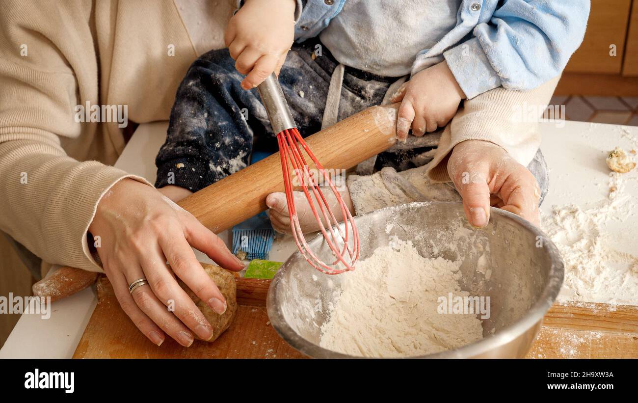 View of Closeup of little baby boy kneading dough and flour in bowl for making ...