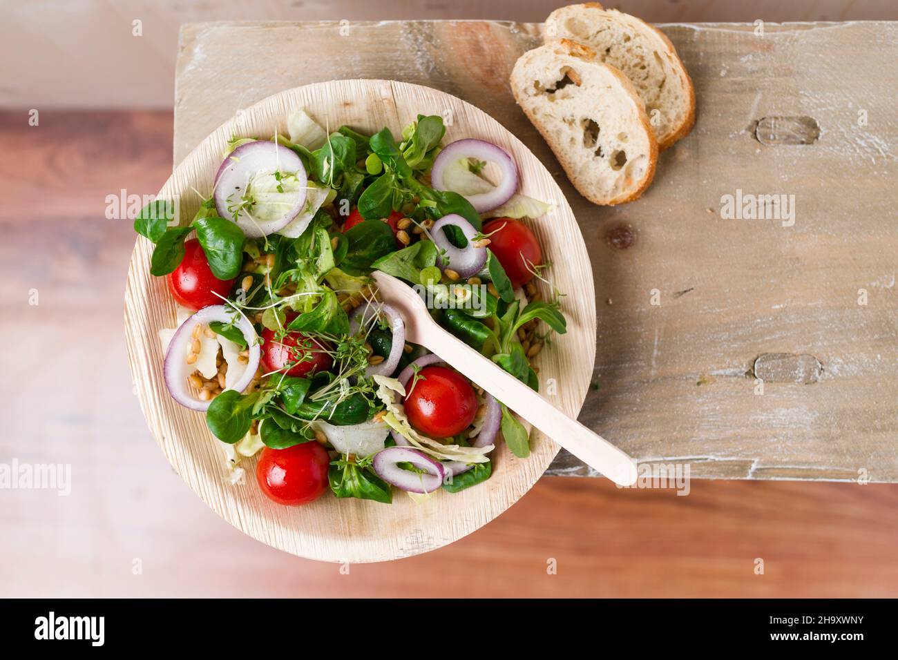 Vegan salad (einkorn wheat, tomatoes, lamb's lettuce, red onion rings, iceberg lettuce, cress, pepper) in a palm leaf bowl Stock Photo