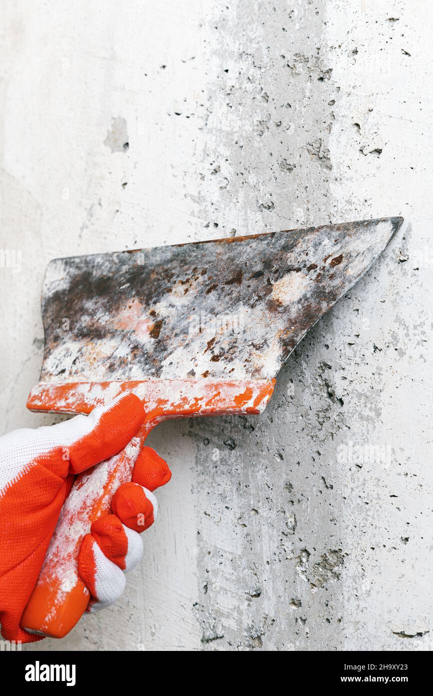 Hand of plasterer holds an old flexible blade spackle knife and scrapes