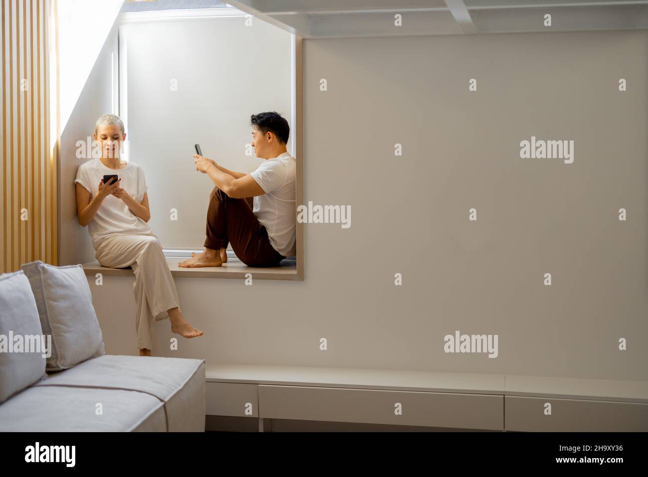 Couple using smartphones on windowsill at home Stock Photo
