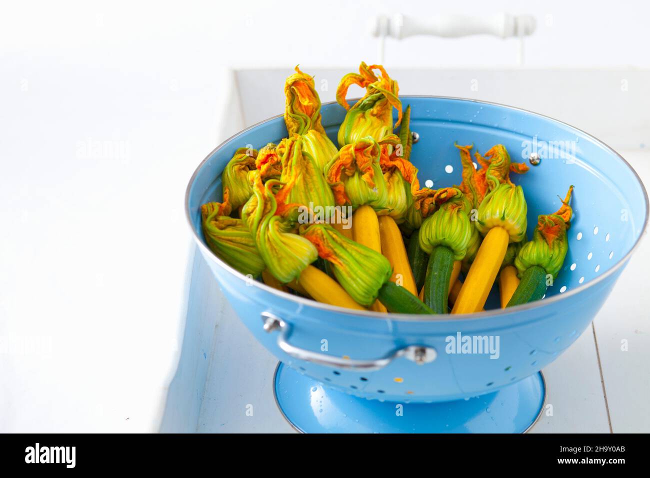 Green and yellow courgettes with flowers in a blue enamel colander