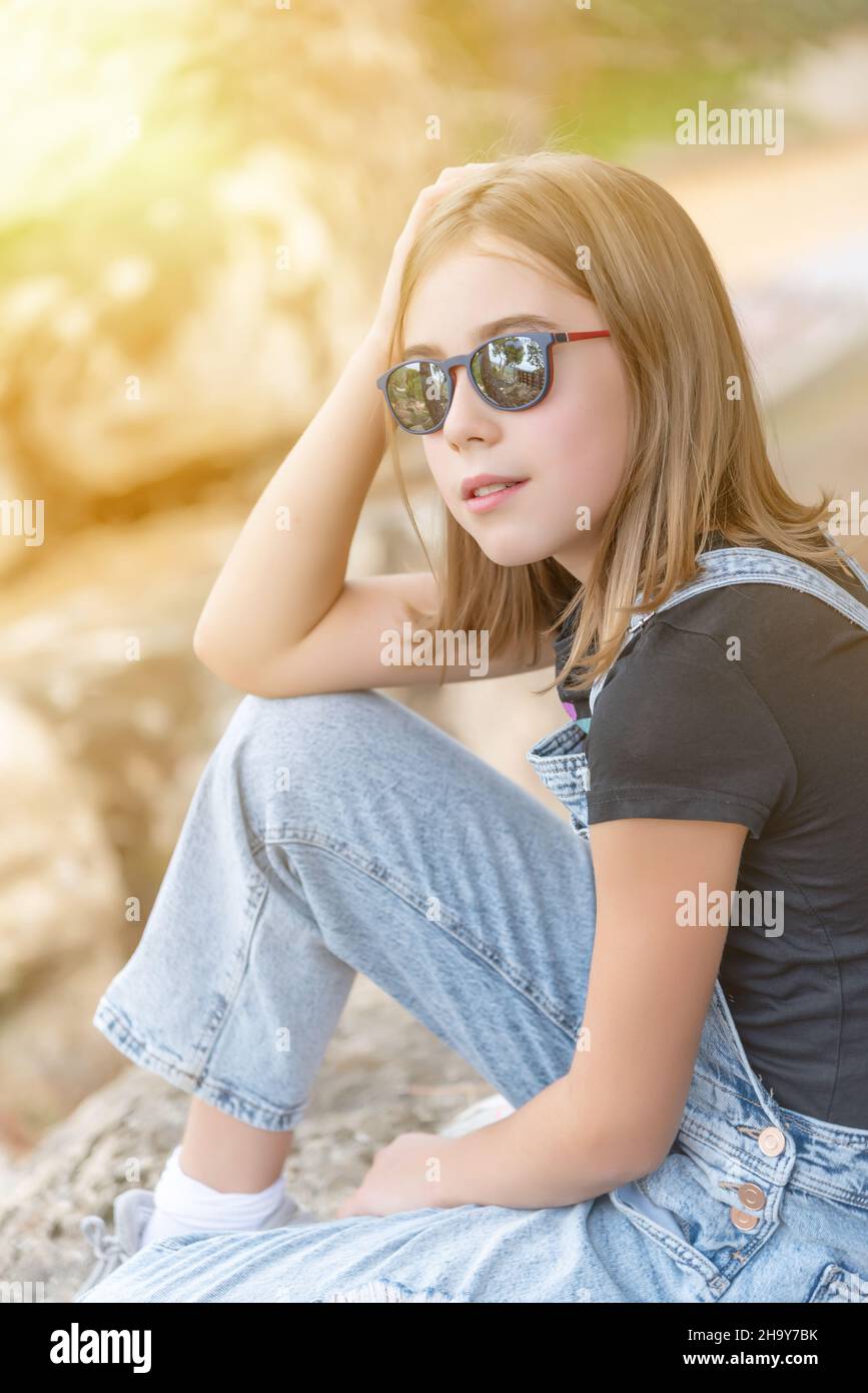 Teenage girl with sunglasses and casual clothes sitting looking at the horizon Stock Photo