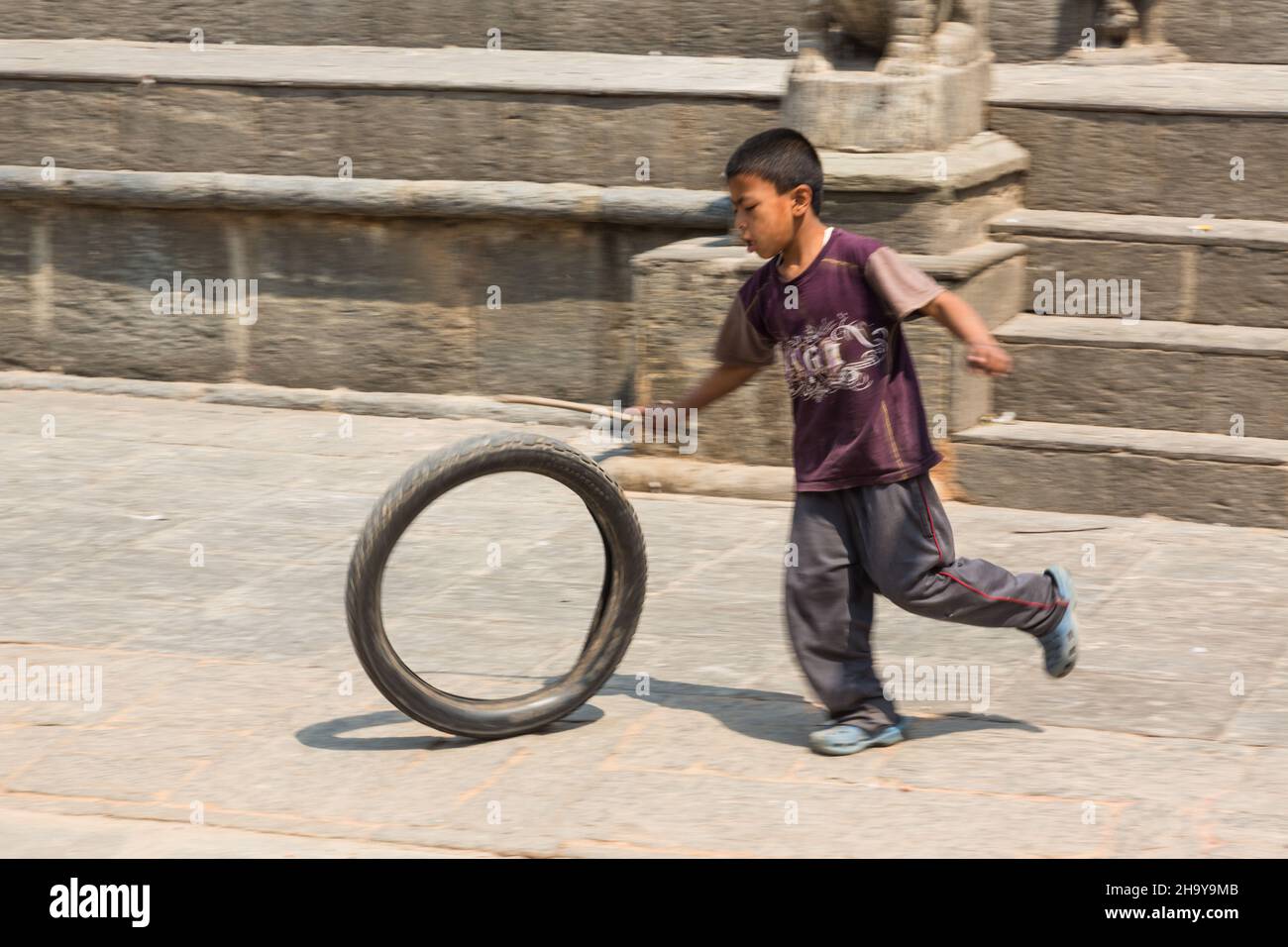A young Newari boy rolls an old motorcycle tire with a stick in the medieval village of Bungamati, Nepal. Stock Photo