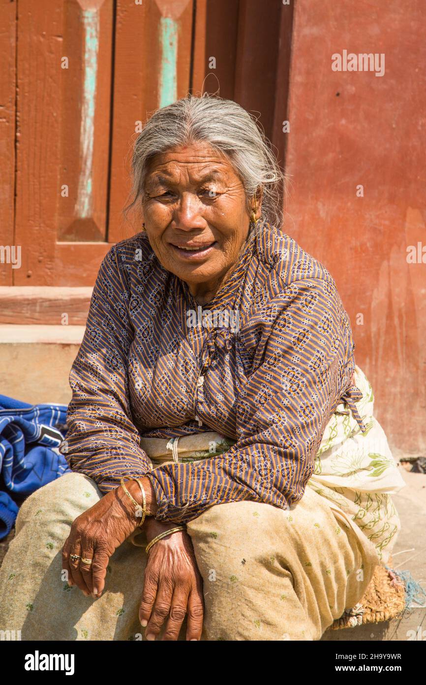 An older Newari woman sits on the sidewalk in front of her home in the medieval Newari village of Bungamati, Nepal Stock Photo