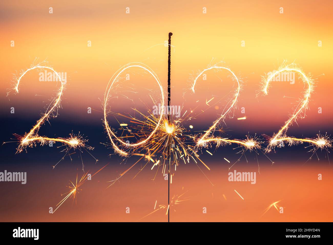 Happy new year 2022 text written with Sparkle firework on sunset background. Bengal flame. Stock Photo