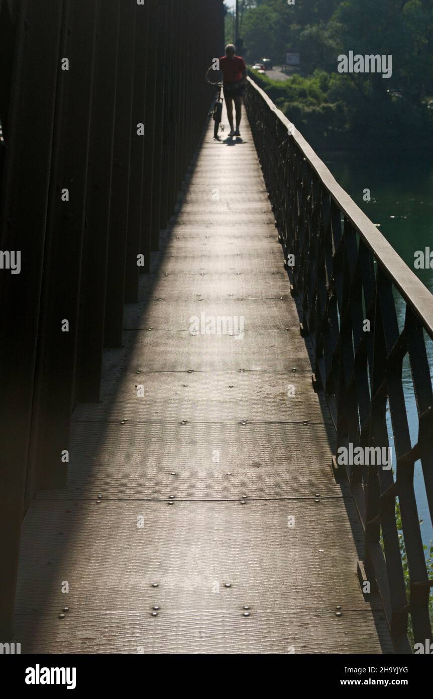 person walking with bicycle on iron river bridge Stock Photo