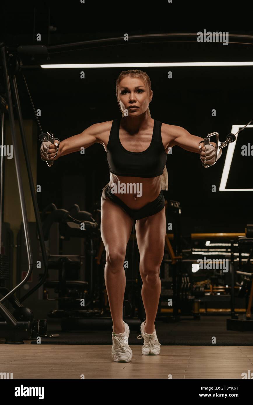 https://c8.alamy.com/comp/2H9YK6T/a-sporty-woman-with-blonde-hair-is-doing-a-chest-workout-on-the-cable-machine-in-a-gym-a-girl-is-training-her-pectoral-muscles-2H9YK6T.jpg