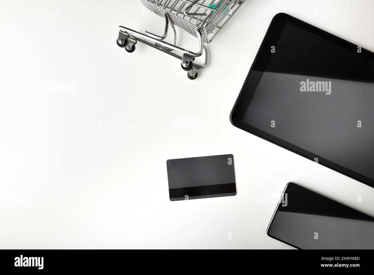 Online payment concept with shopping cart credit card and devices on white table. Top view. Horizontal composition. Stock Photo