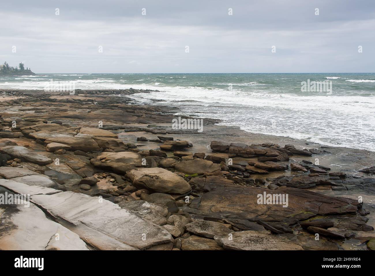 The wind is getting stronger and the waves splash to the shore on the rocky beach. Stock Photo