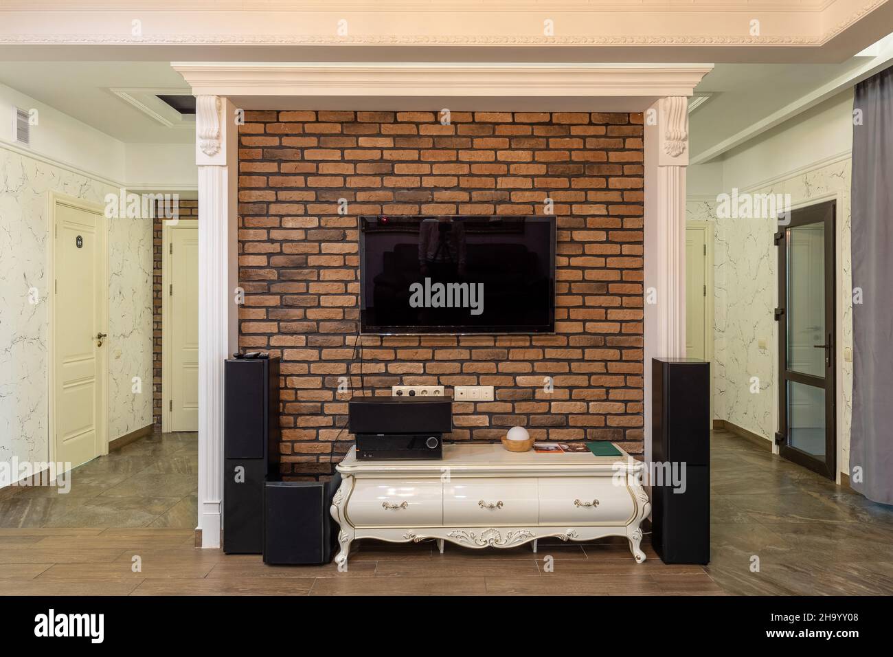 living room interior with a large TV and a home theater that hangs on the wall made of artificial bricks, a room in light shades with dark tiles on Stock Photo