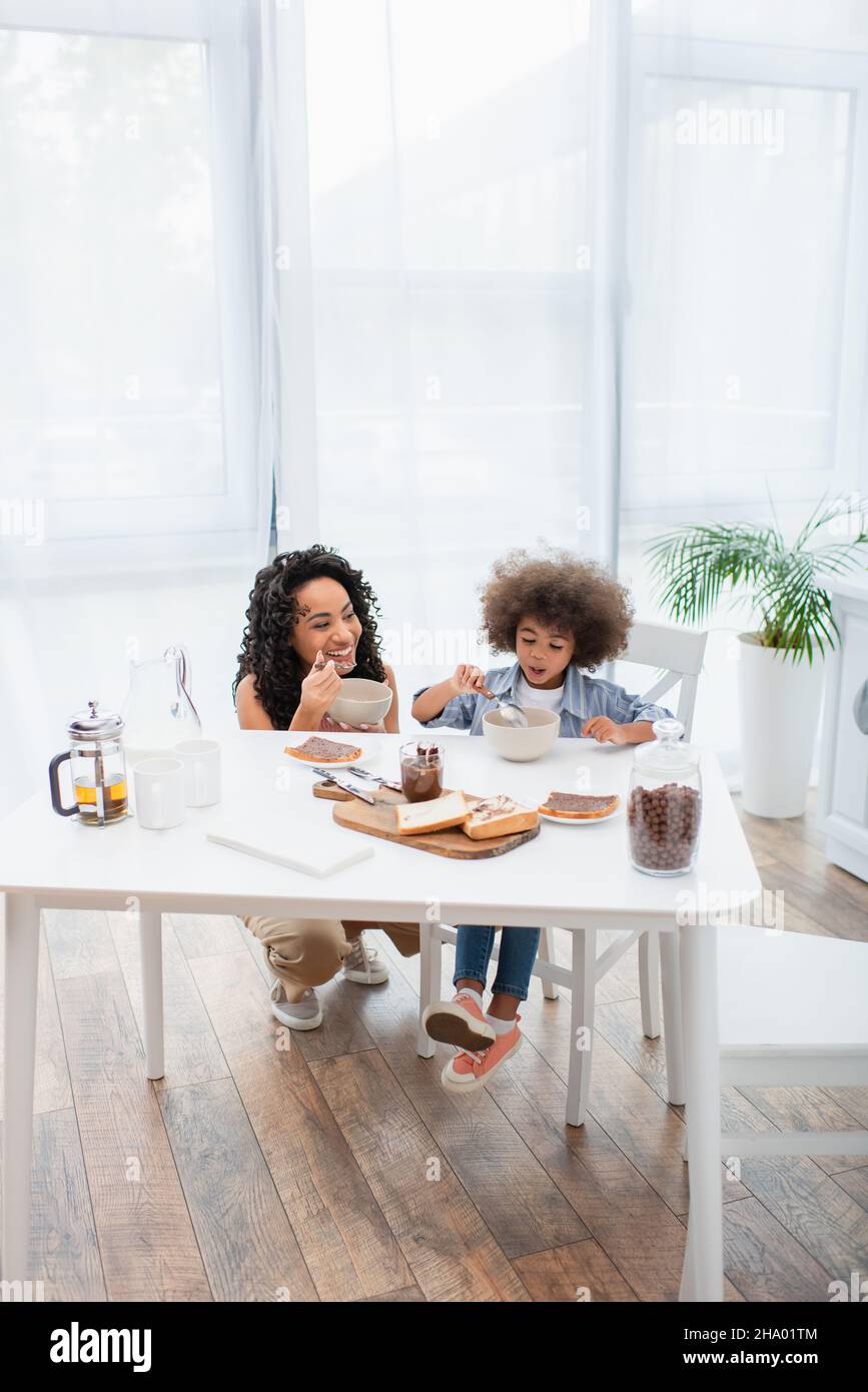 Smiling african american family eating breakfast near milk and tea in kitchen Stock Photo