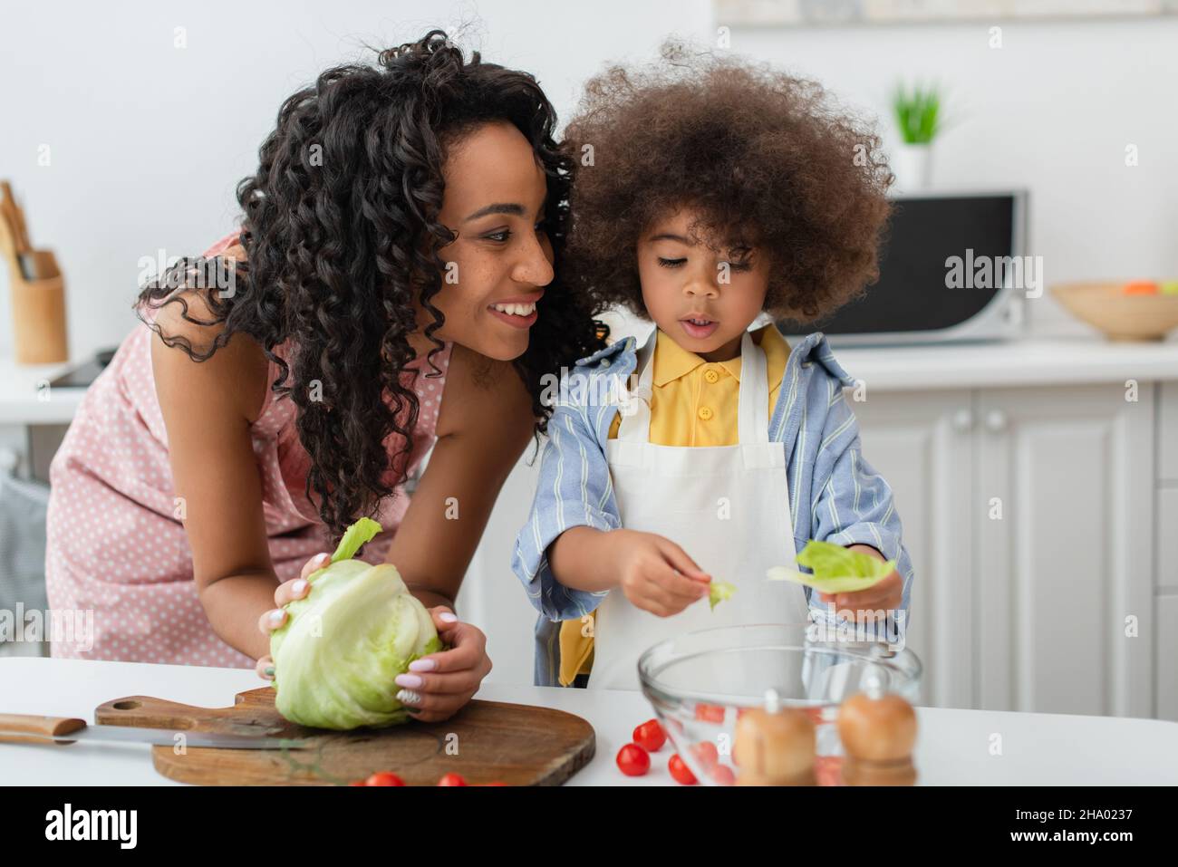 Smiling african american woman holding cabbage near daughter in apron ...