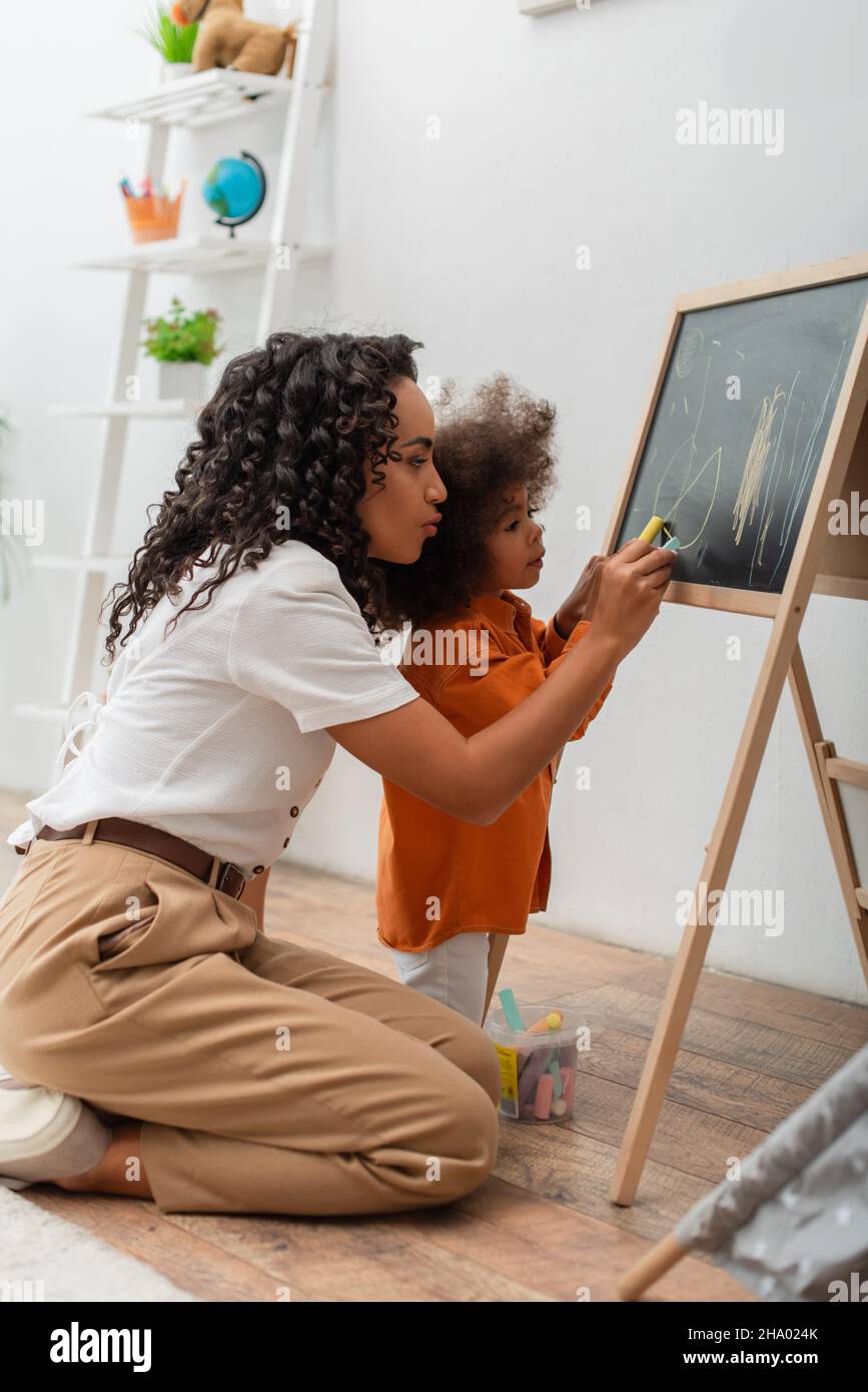 Young african american woman drawing on chalkboard with daughter at home Stock Photo