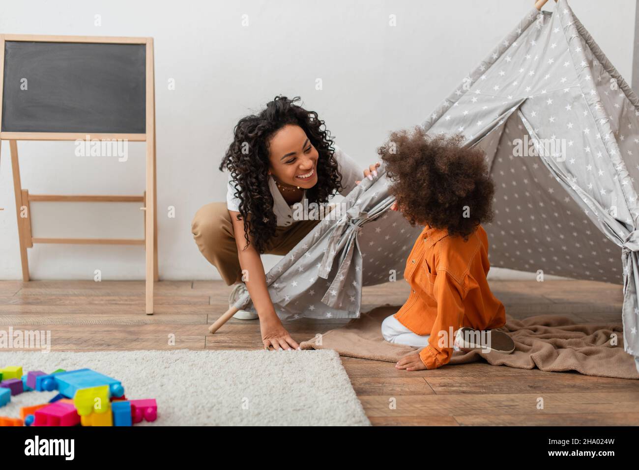 Smiling african american mother looking at child in teepee at home Stock Photo
