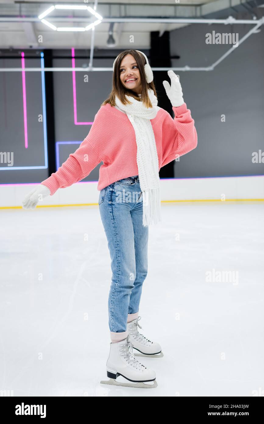 full length of happy woman in white ear muffs and winter outfit skating