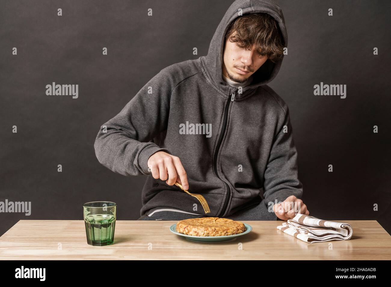 Young man sitting at the table eating a potato omelette with chorizo Stock Photo