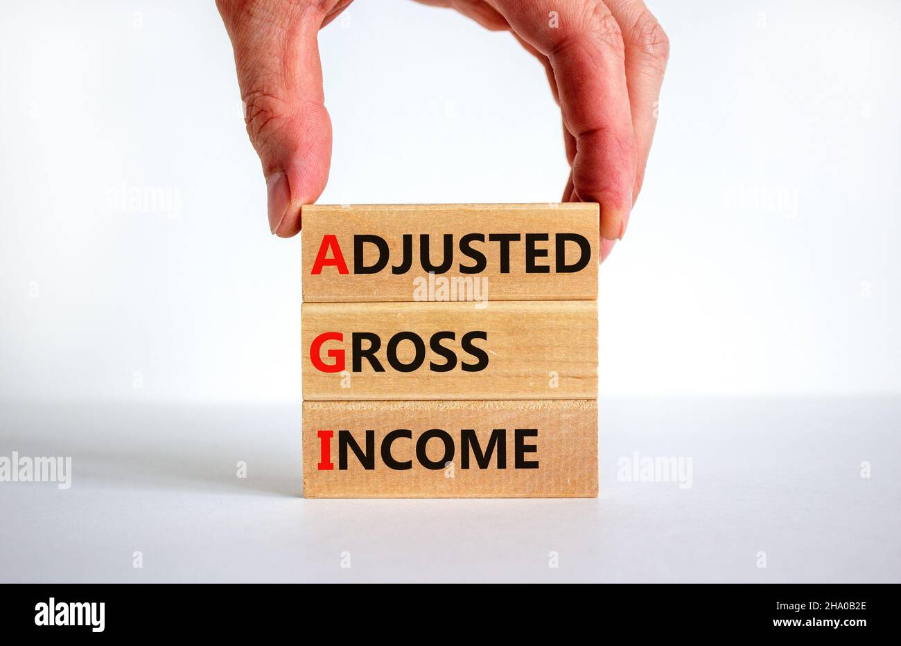AGI adjusted gross income symbol. Concept words AGI adjusted gross income on wooden blocks. Beautiful white background, businessman hand, copy space. Stock Photo