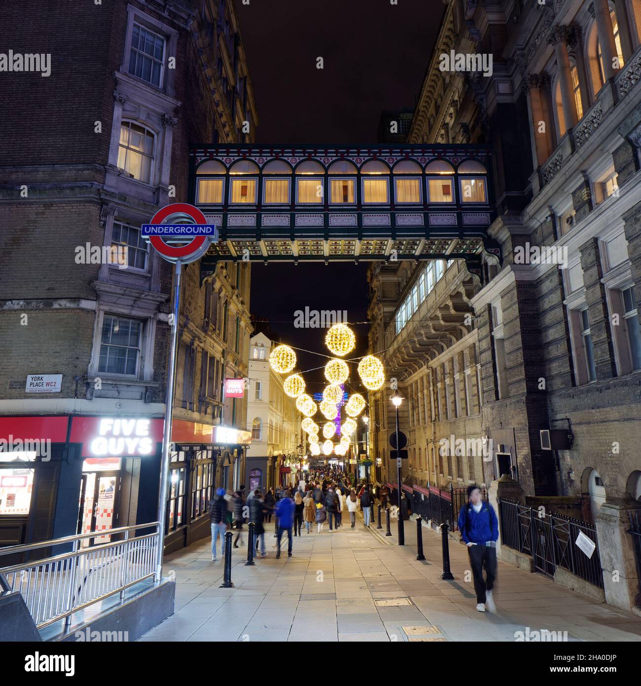 Illuminated raised walkway on Villiers Street near Charing Cross station on the right with an Underground Sign and festive lights. London. Stock Photo