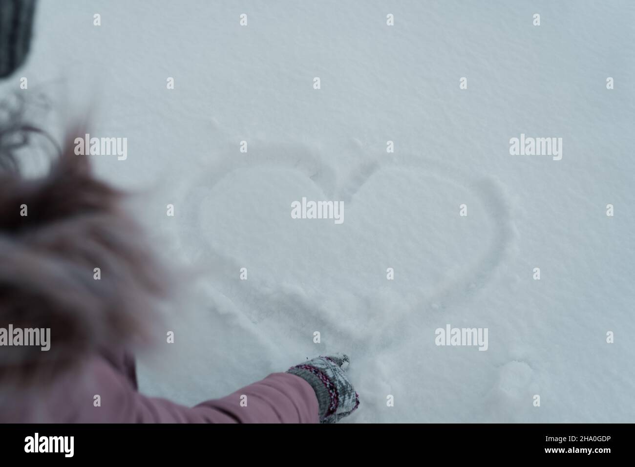 a girl in a pink jacket draws a heart in the snow,love is all around us,love melts ice Stock Photo