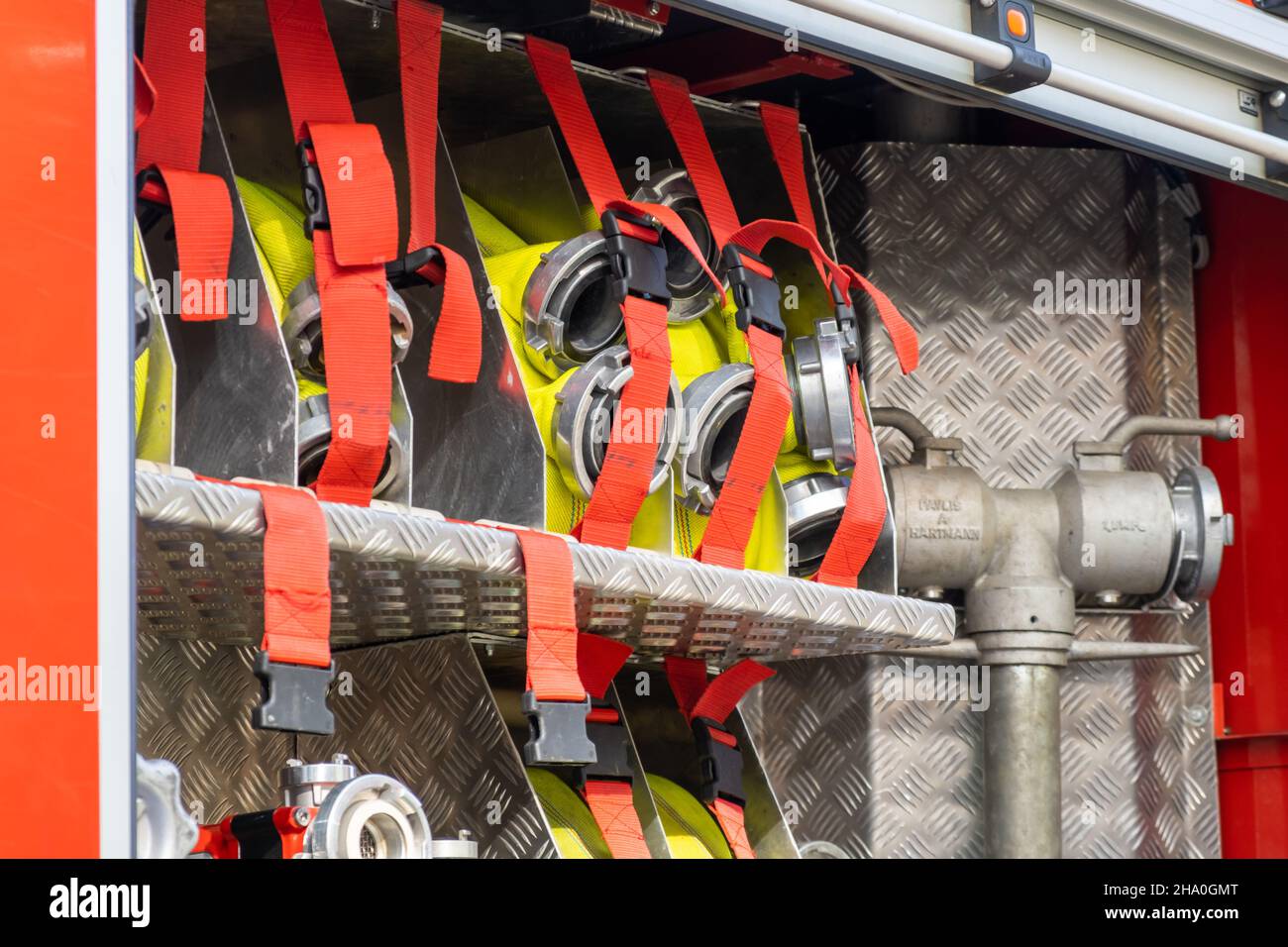 Rolled yellow hoses fastened in cells by belts with clamps in open fire truck metal body at contemporary station close view Stock Photo