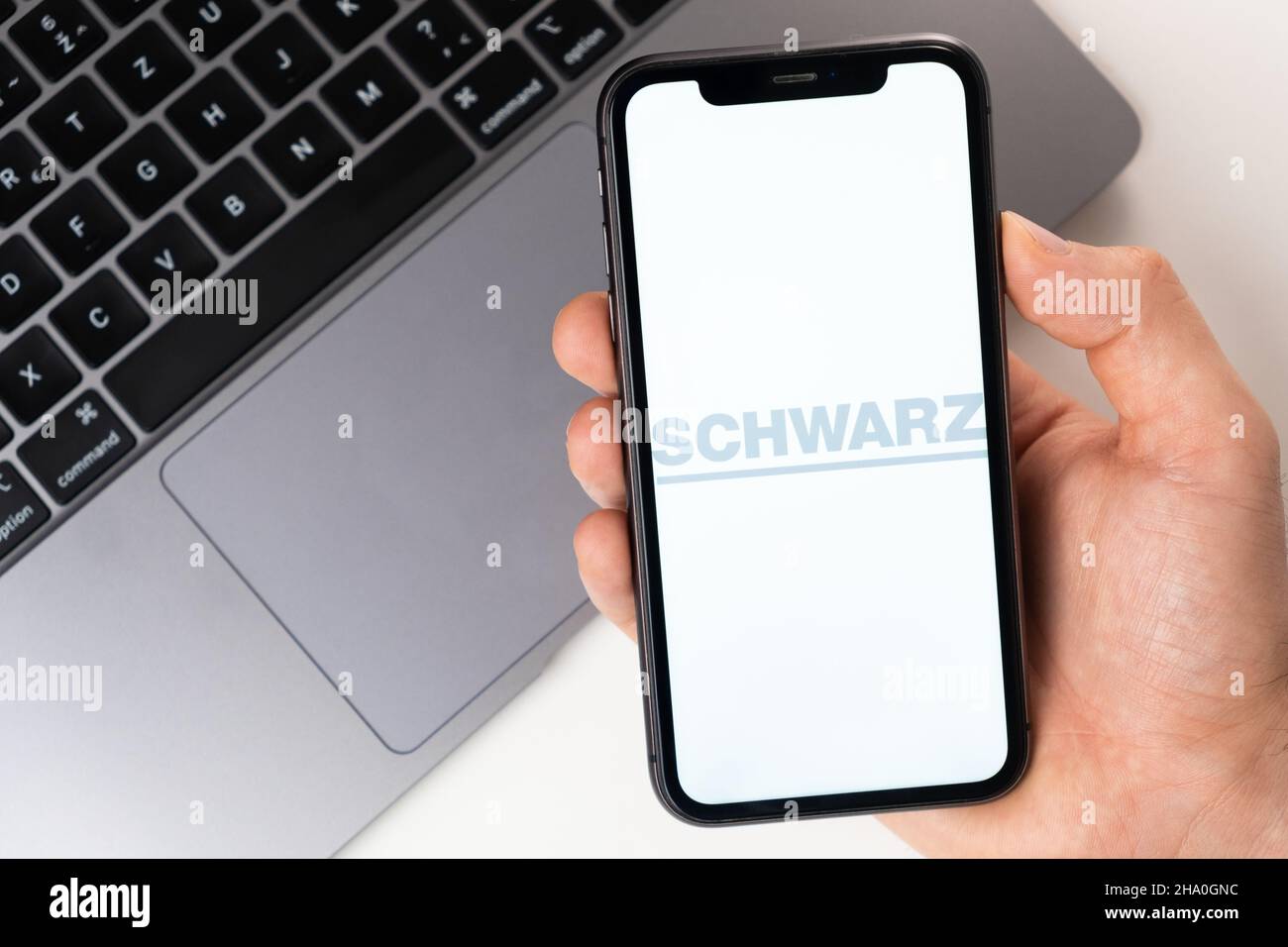 SCHWARZ mobile application on the smartphone screen. A mobile phone in a man hand near an open laptop. White background. November 2021, San Francisco, USA Stock Photo